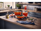 Marmites et poêles orange en fonte sur une cuisinière à gaz dans une cuisine moderne.