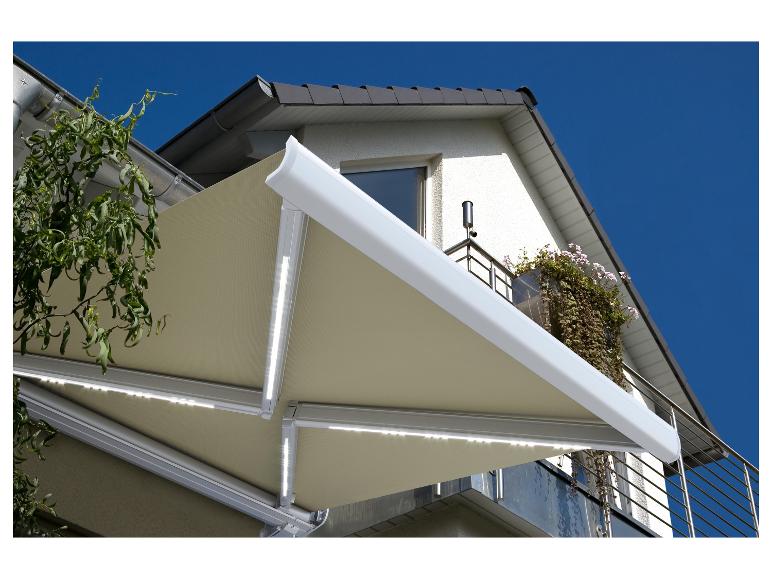 Store banne beige avec éclairage LED au-dessus d'un balcon fleuri sous un ciel bleu.