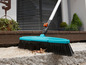 Un balai bleu avec un long manche, idéal pour nettoyer les jardins et les terrasses.