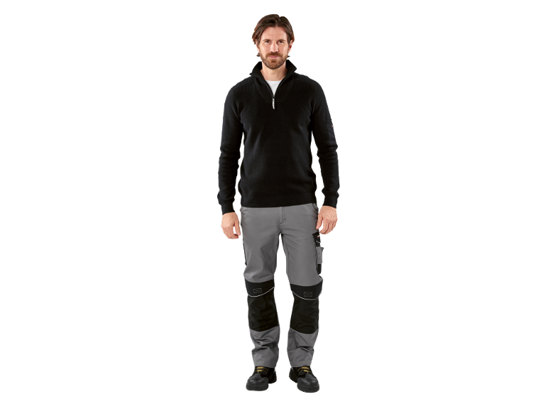 Homme portant un pull de travail noir zippé, un pantalon de travail gris et des chaussures de sécurité noires