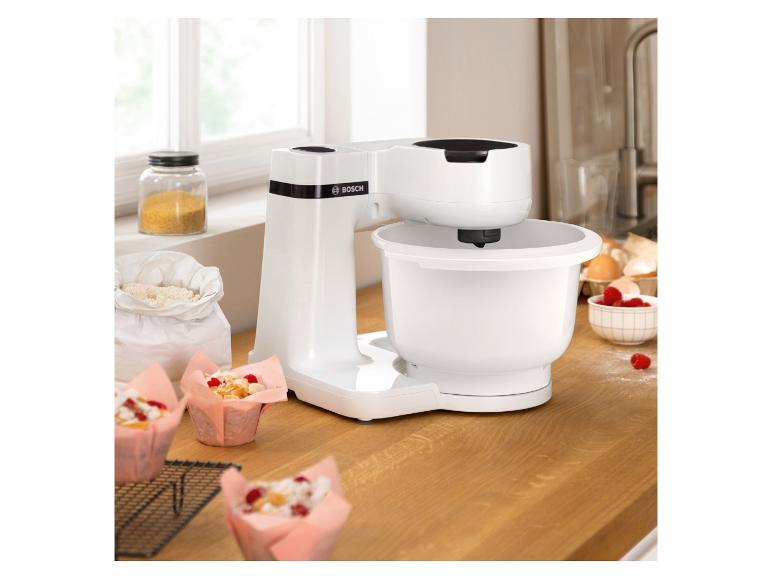 Un robot pâtissier Bosch blanc avec des muffins et des baies sur un comptoir en bois.