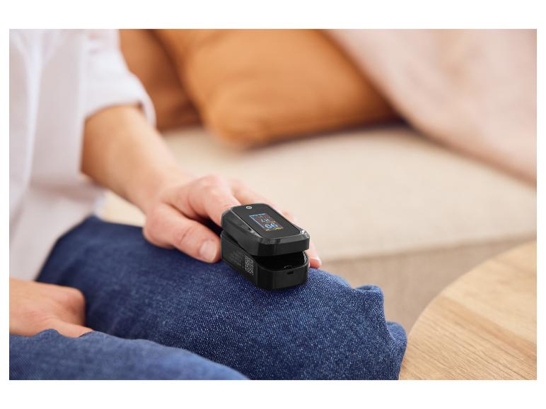 Personne assise sur un canapé, mesurant le niveau d'oxygène sanguin et la fréquence cardiaque avec un oxymètre de pouls.