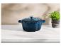 Une cocotte en fonte bleue avec couvercle sur un comptoir en marbre blanc à côté d'une plante en pot.