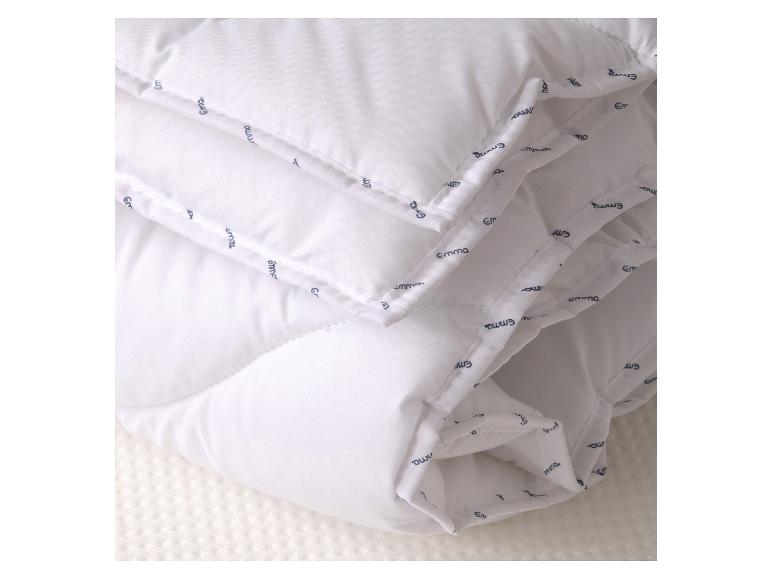 Couette blanche matelassée avec une bordure à motifs, posée sur une surface blanche texturée.