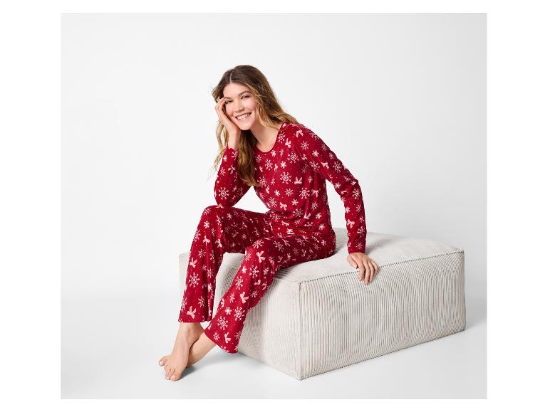 Femme souriante en pyjama de Noël rouge avec des flocons de neige et des nœuds, assise sur un pouf.