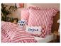 Chambre avec literie rayée rouge et blanche et coussins avec les textes « BLAH BLAH » et « Bonjour ».