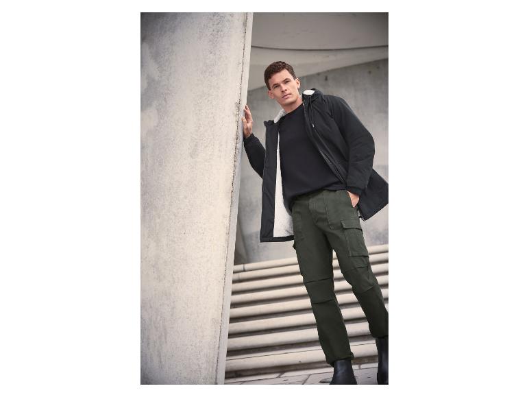 Homme en veste noire doublée de blanc, t-shirt noir et pantalon cargo vert.