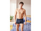 Homme en boxer bleu foncé, debout dans la chambre.