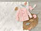 Un cardigan rose pour bébé sur un tapis blanc avec des feuilles d'automne.
