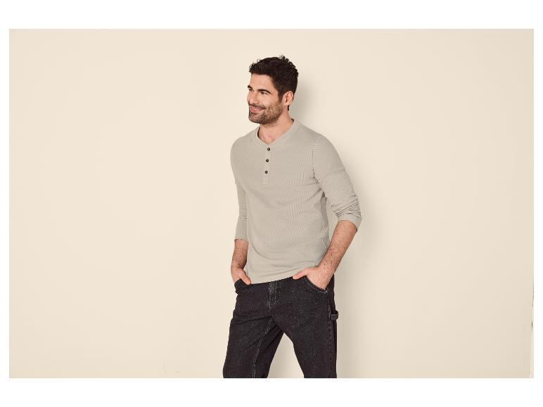 Homme en chemise Henley gris clair à manches longues et jean foncé, mains dans les poches.