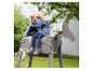 Deux enfants jouent sur un cheval à bascule en bois dans un jardin.