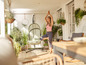 Une femme fait du yoga sur une terrasse avec un fauteuil suspendu et une table en bois.