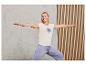 Une femme portant un t-shirt blanc avec l'inscription 'state of mind' et un pantalon violet, fait du yoga.