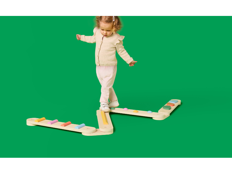 Enfant en bas âge en équilibre sur une poutre en bois avec des marches colorées.