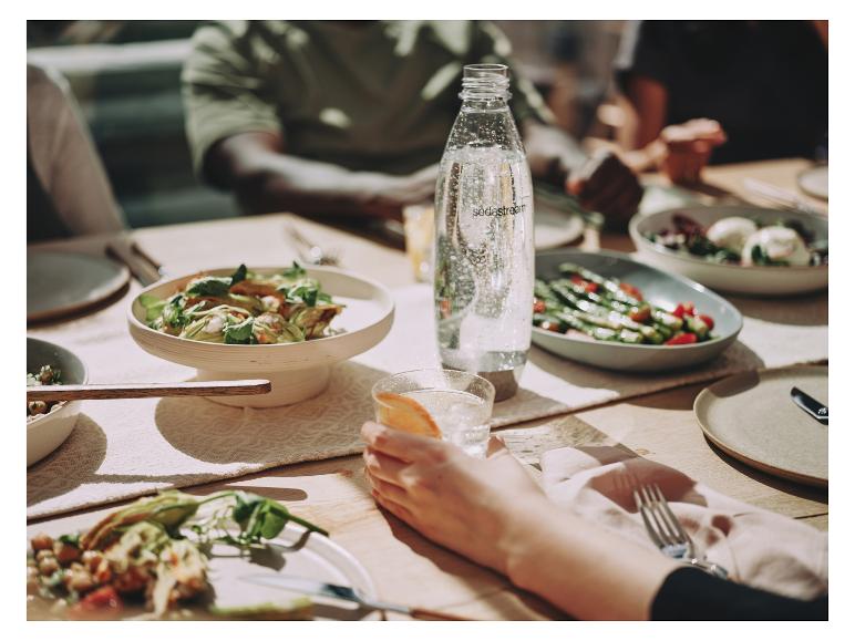 Une bouteille Sodastream d'eau pétillante sur une table avec de la nourriture et des gens.