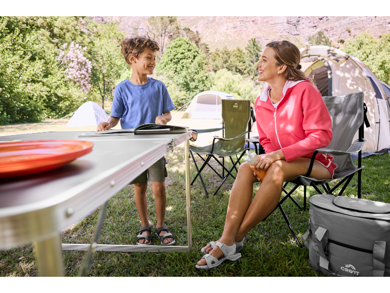 Femme et enfant en camping avec une table pliante, des chaises de camping et des tentes.