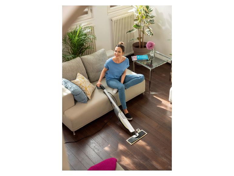 Femme sur un canapé nettoyant un parquet avec un nettoyeur de sol.