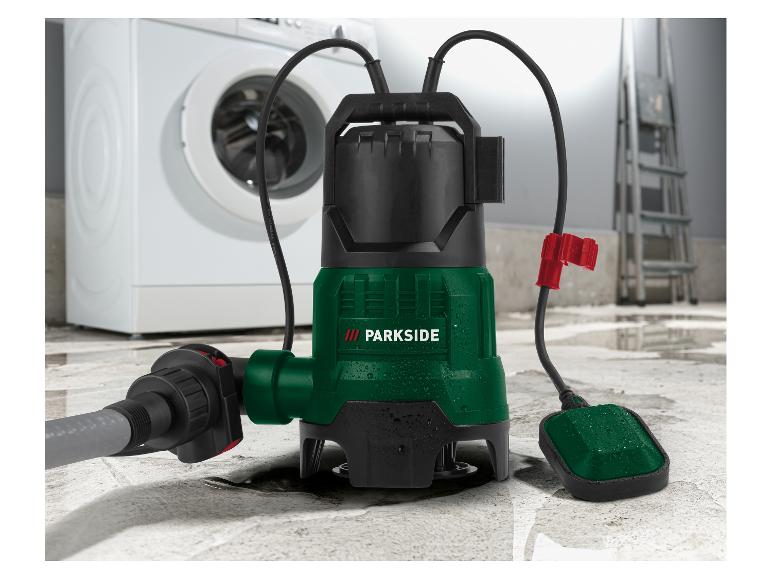 Une pompe submersible avec un tuyau et un interrupteur à flotteur sur un sol mouillé, avec une machine à laver en arrière-plan.