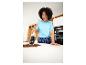 Femme avec un aspirateur à main nettoyant du café renversé sur un comptoir de cuisine.