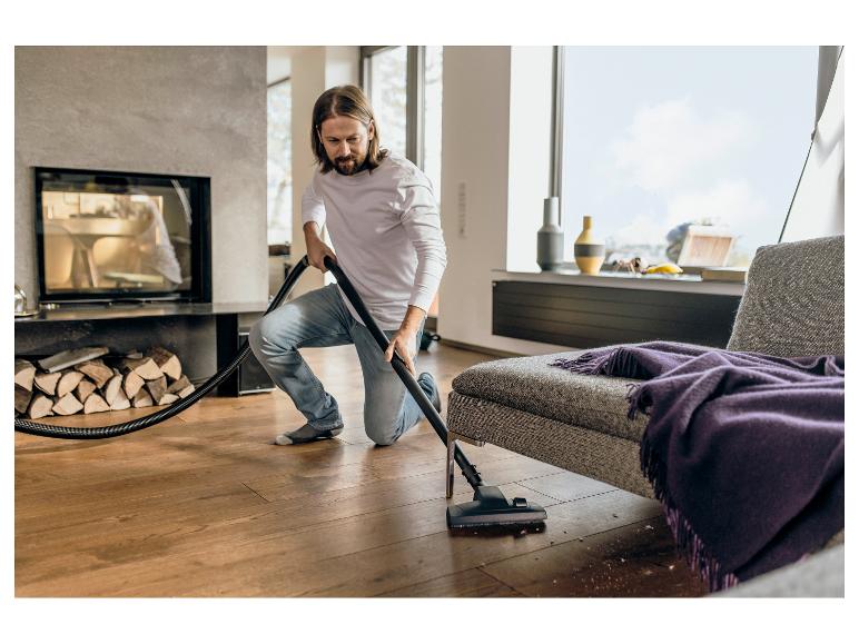 Homme passant l'aspirateur sur un parquet dans un salon moderne avec cheminée.