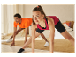 Deux personnes font des étirements dans leurs vêtements de sport à la maison.