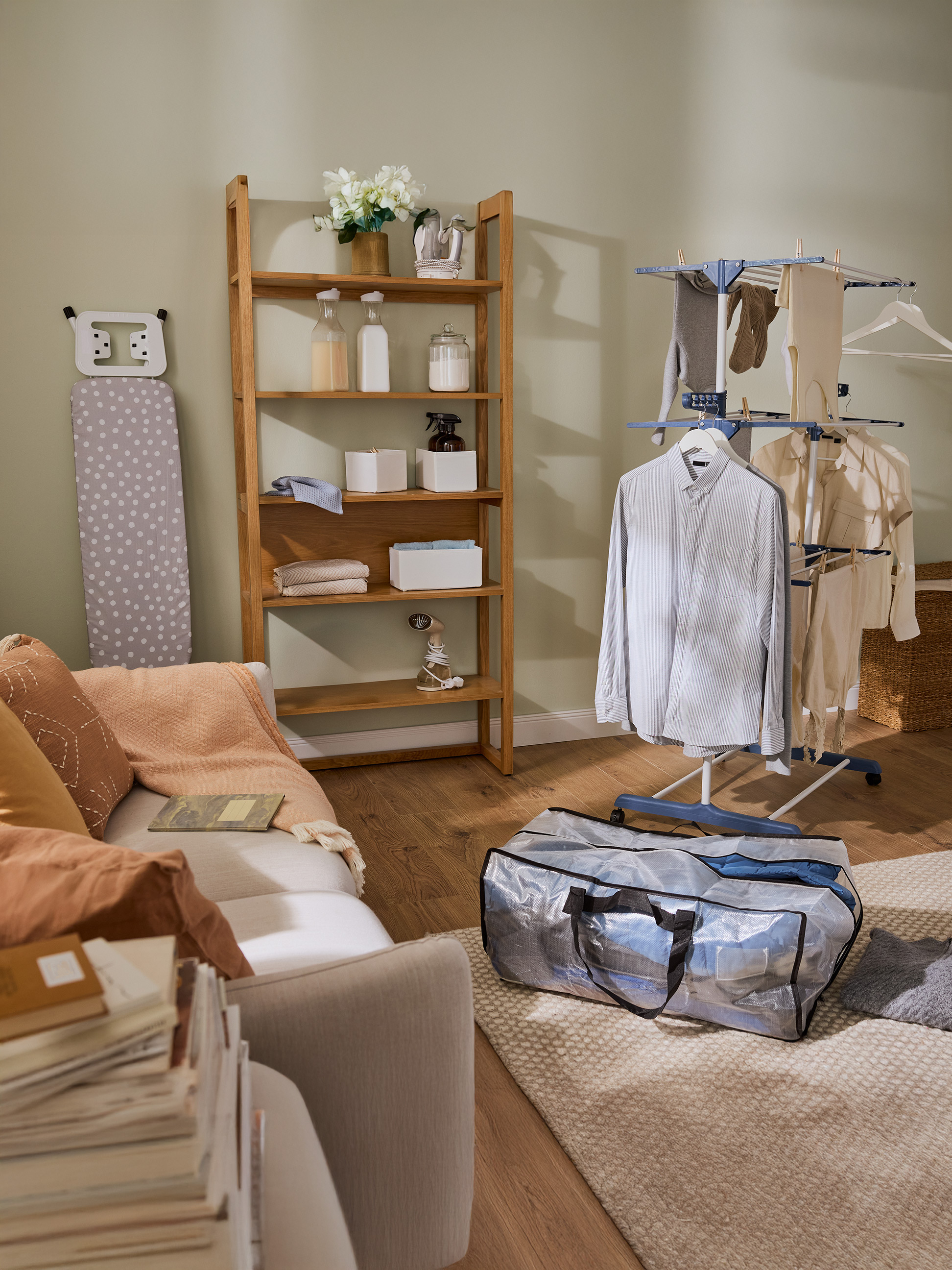 Buanderie avec étagère en bois, planche à repasser et étendoir à linge avec vêtements.