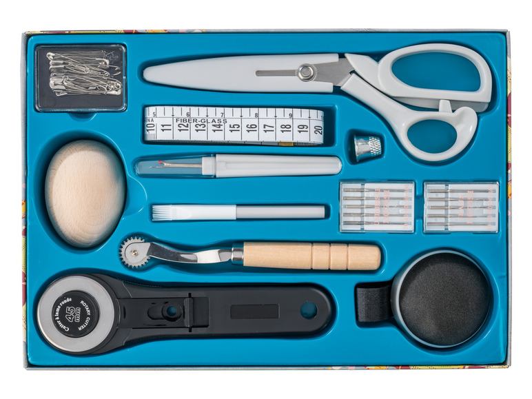 Un kit de couture avec un cutter rotatif, des ciseaux, des aiguilles et un ruban à mesurer.