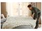 Un homme étendant une couverture premium blanche LIVARNO home sur un lit.