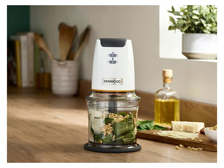 Hachoir blanc avec ingrédients pour pesto sur un comptoir de cuisine en bois.