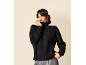 Femme souriante portant un pull à col roulé en maille noire et un pantalon gris.