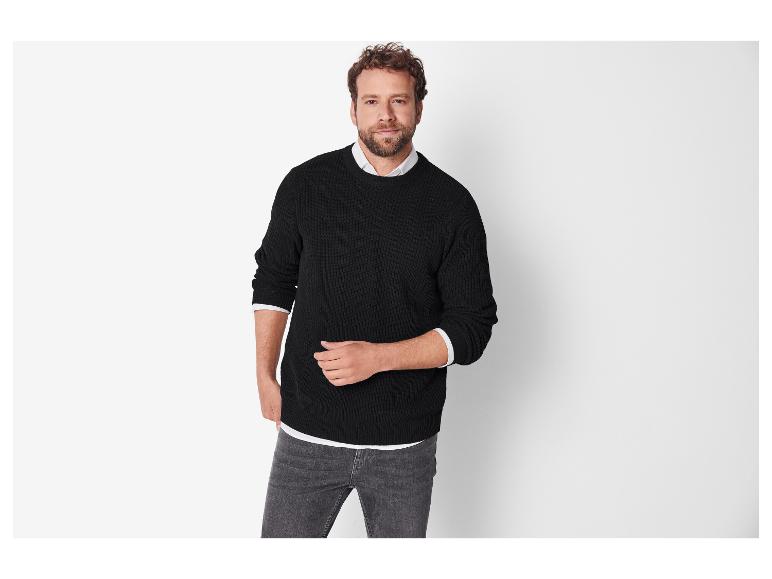 Un homme en pull noir et jean gris.