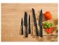 Ensemble de couteaux noirs sur une planche à découper en bois avec tomate et basilic.