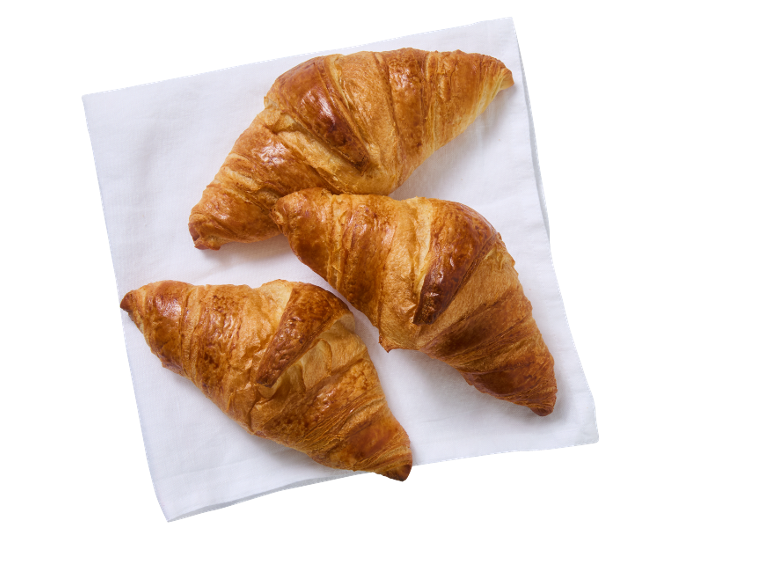 Trois croissants dorés sur une serviette blanche, vue de dessus.