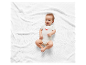 Bébé souriant vêtu d'un body blanc à motif crabe sur un plaid blanc.