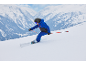 Enfant en tenue de ski bleue et noire, casque et lunettes, dévalant une piste de ski enneigée.