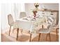 Une table dressée avec une nappe à motifs floraux et des chaises blanches.