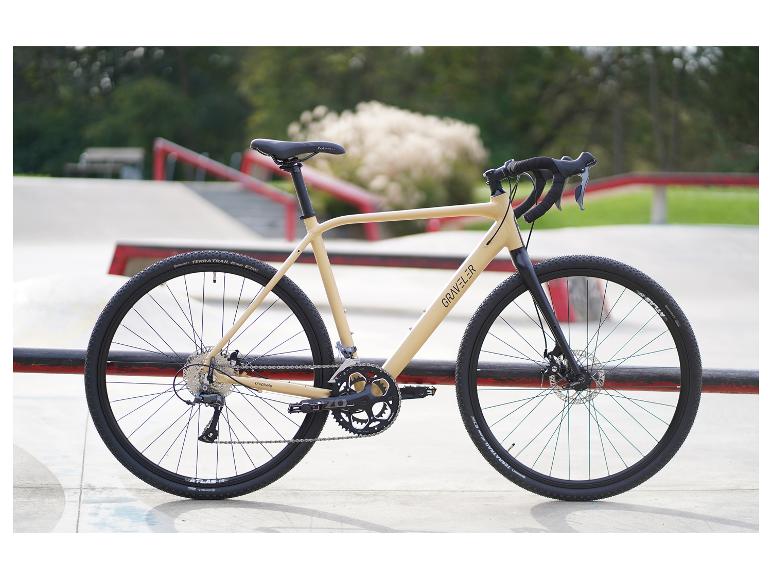Vélo de gravel GRAVELER beige avec pneus et guidon noirs, garé dans un skatepark.