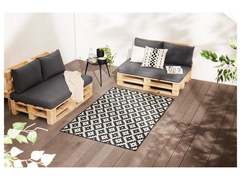 Deux bancs en palettes avec des coussins et un tapis noir et blanc sur une terrasse en bois.