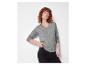 Femme aux cheveux bouclés portant un pull gris et un jean noir.