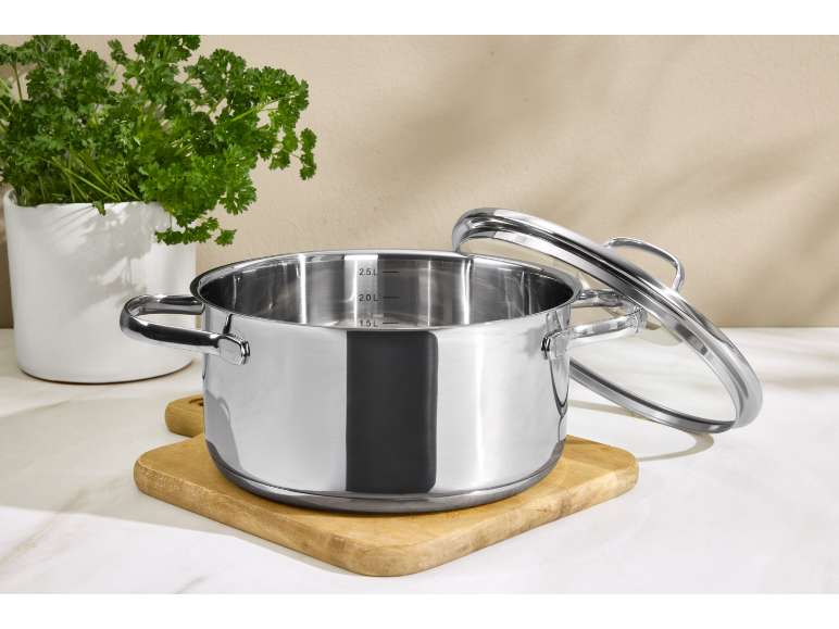 Casserole en acier inoxydable avec couvercle en verre sur une planche à découper en bois.