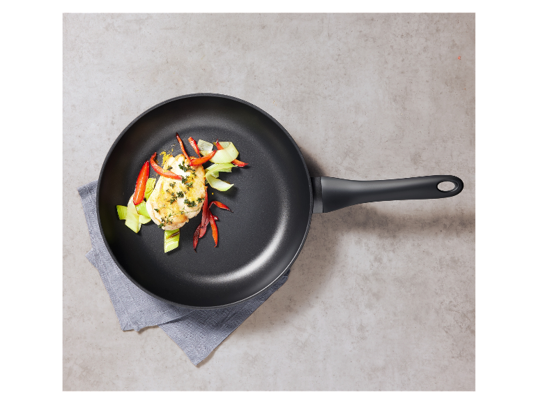 Une poêle noire avec du poulet et des légumes grillés.