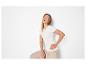 Femme souriante en t-shirt blanc côtelé et pantalon beige, posant la main sur la hanche.