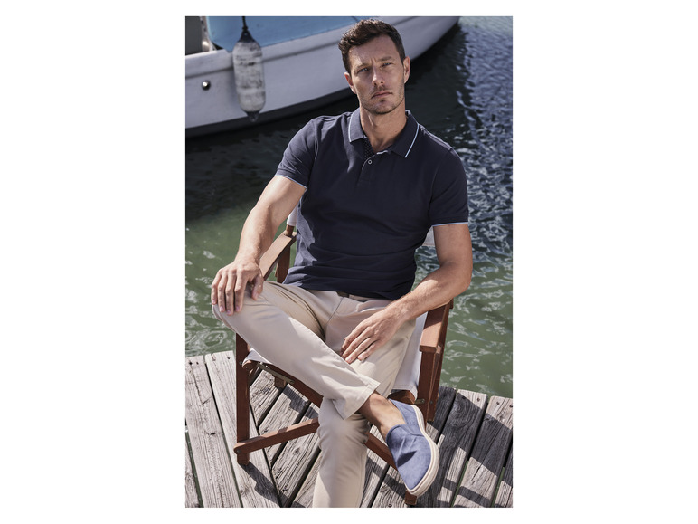 Homme en polo bleu foncé et pantalon beige assis sur une jetée en bois.