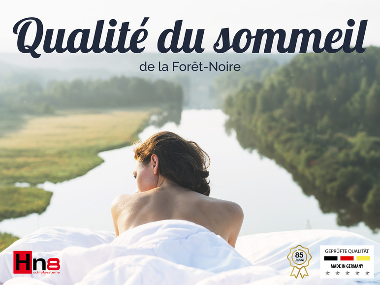 Une femme dans un lit avec le système de sommeil Hn8, avec un certificat 'Geprüfte Qualität', dans un paysage naturel.