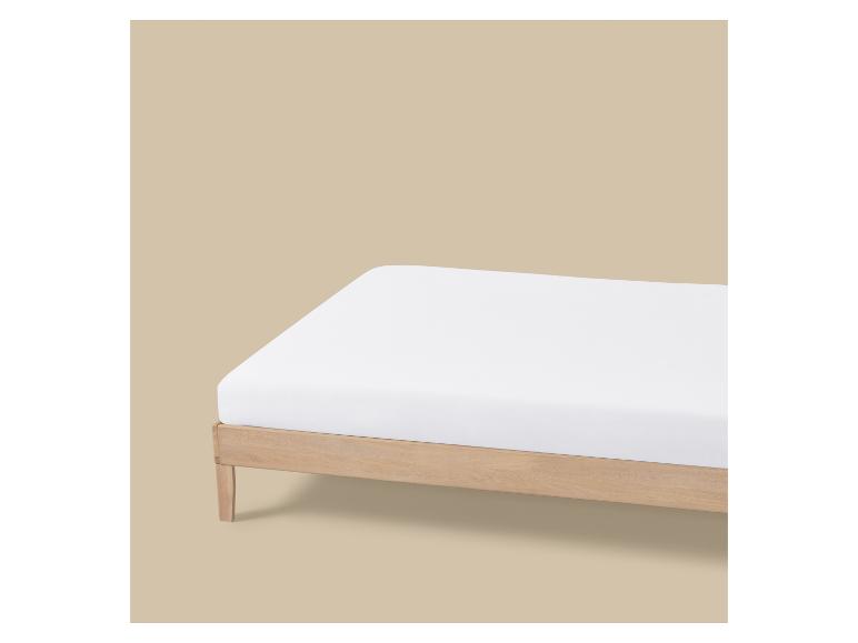 Drap-housse blanc sur un lit en bois clair sur fond beige.