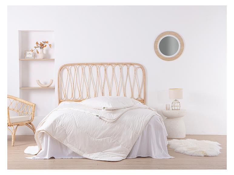 Chambre avec lit en rotin, couette et oreiller blancs, avec miroir rond et tapis en peau de mouton.
