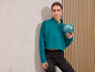 Une femme portant un sweat turquoise et un legging noir tient un ballon de sport.