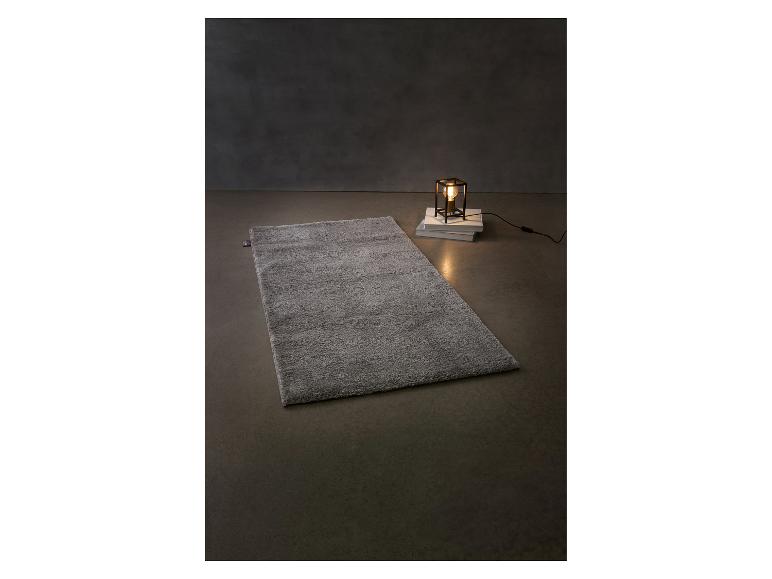 Tapis gris moelleux et lampe de table sur des livres sur fond sombre.