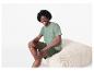 T-shirt et short homme vert olive, assis sur un pouf en velours côtelé beige.