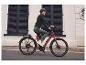 Femme conduisant un vélo électrique rouge bordeaux.